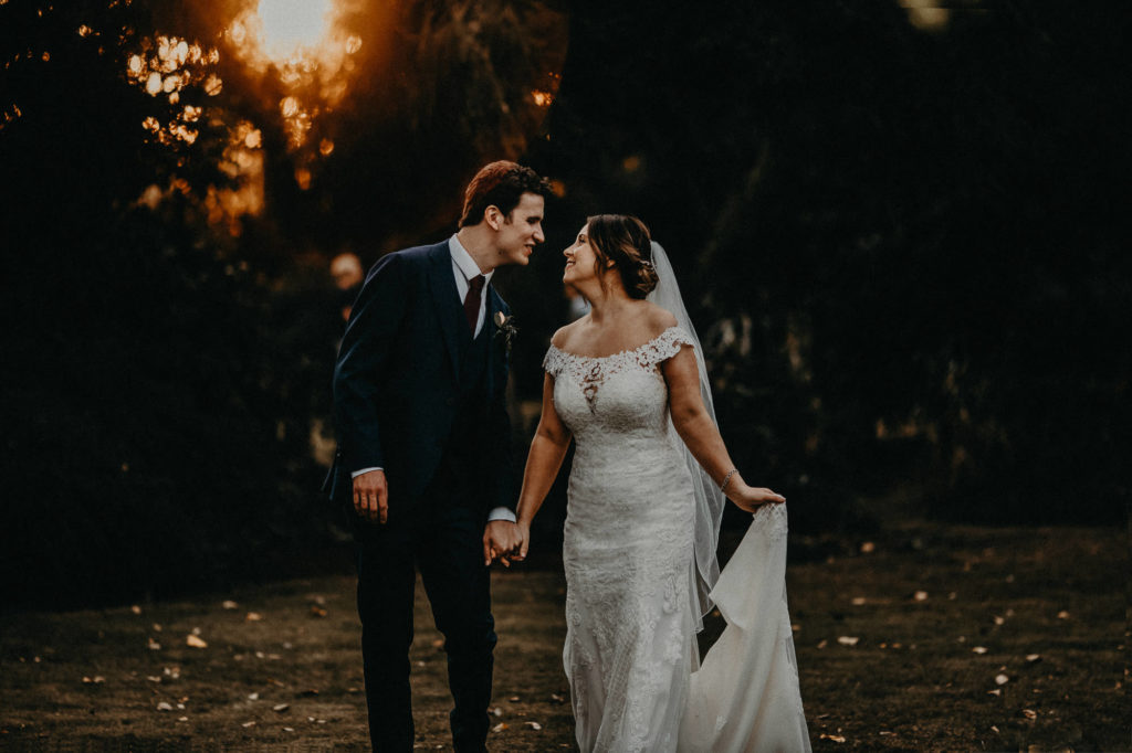 bride during golden hour holding her dress whilst walking and looking at her groom