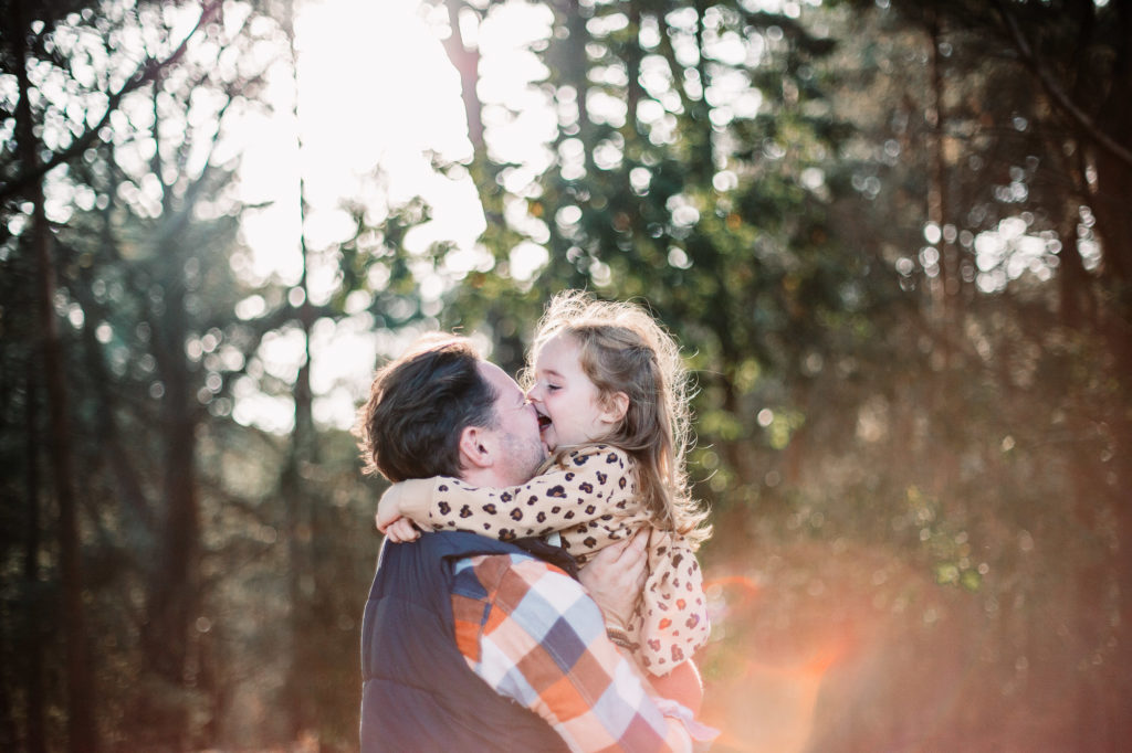 daughter hugging and kissing her father in his arms whilst laughing together and wearing wellie boots