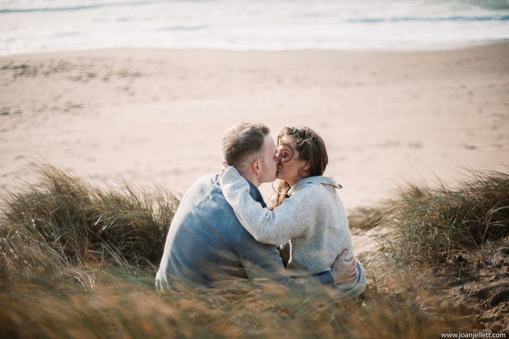 backshot image of engaged couple kissing on top of a sand dune