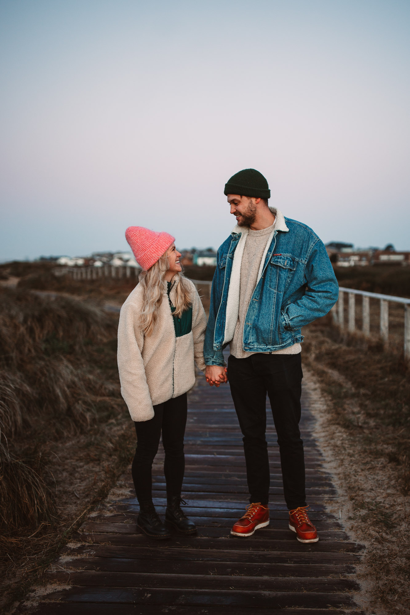 couple holding hands wearing a hat and a denim jacket on their way to watch the sun rise