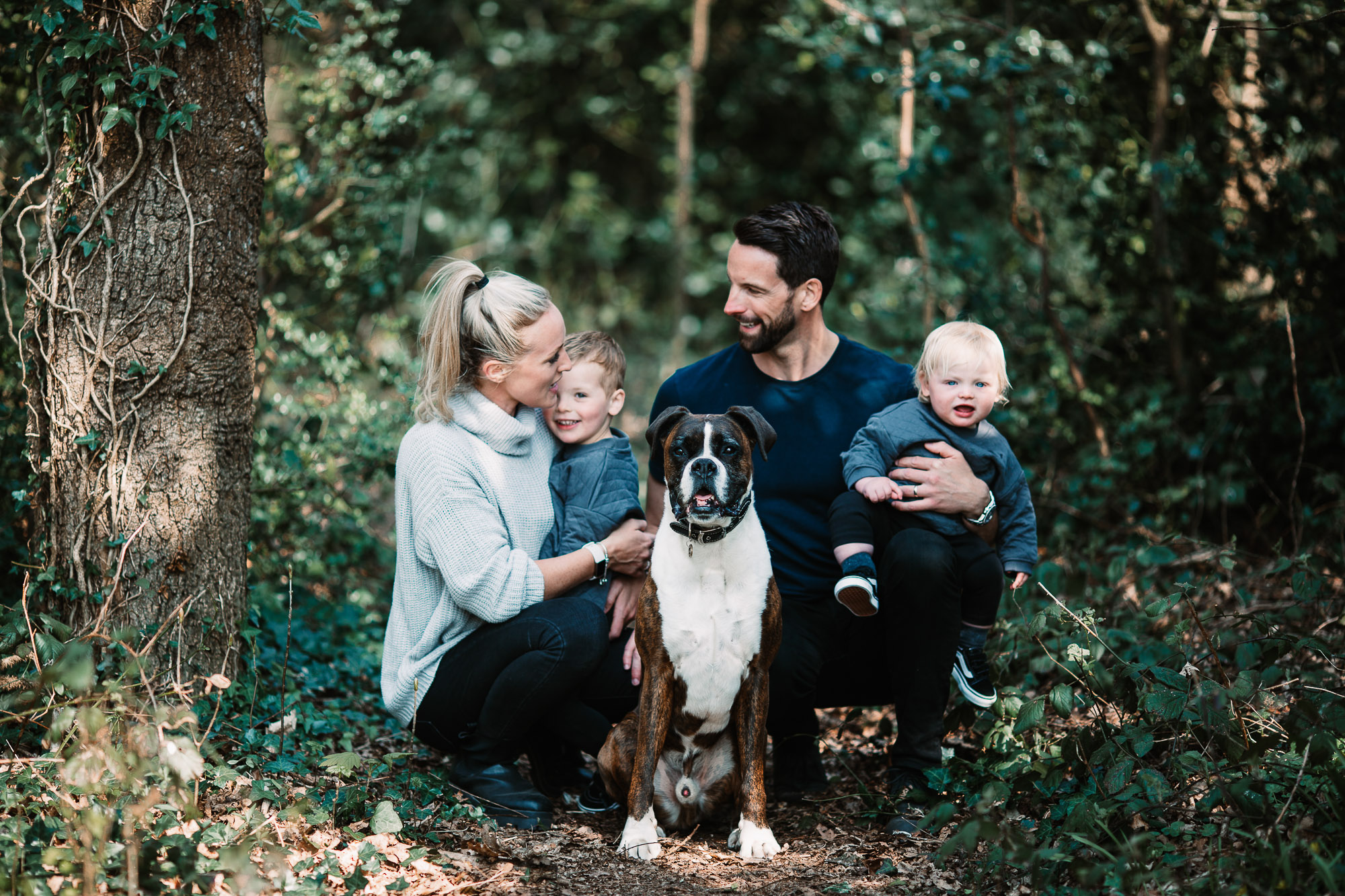 family sat down in the forest in Christchurch having a family picture taken with their dog at the front.