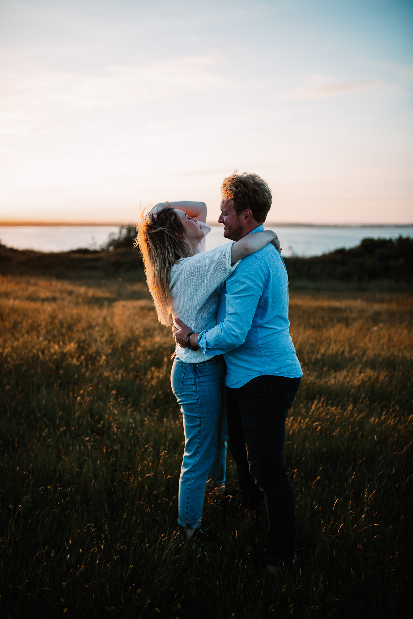 woman touching her hair whilst boyfriend hugs her in the golden hour
