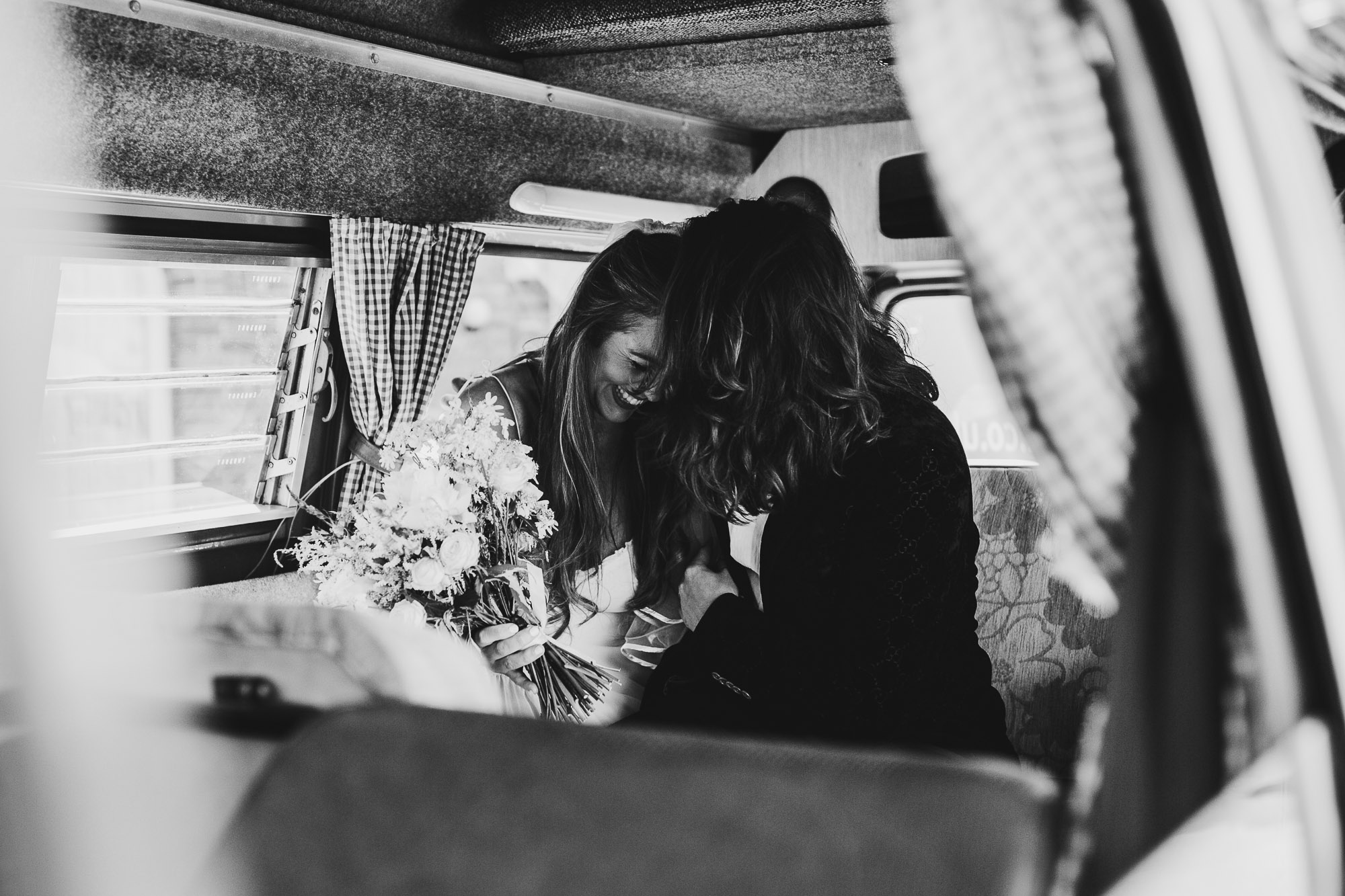 black and white shot of bride and groom laughing inside their car