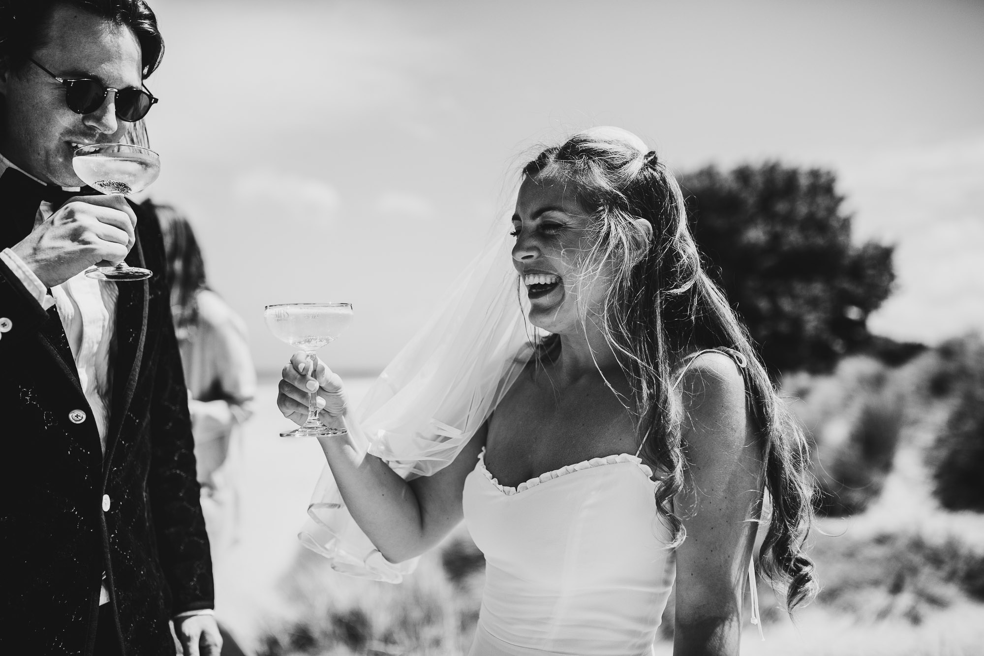 black and white shot of bride and groom laughing and drinking champagne