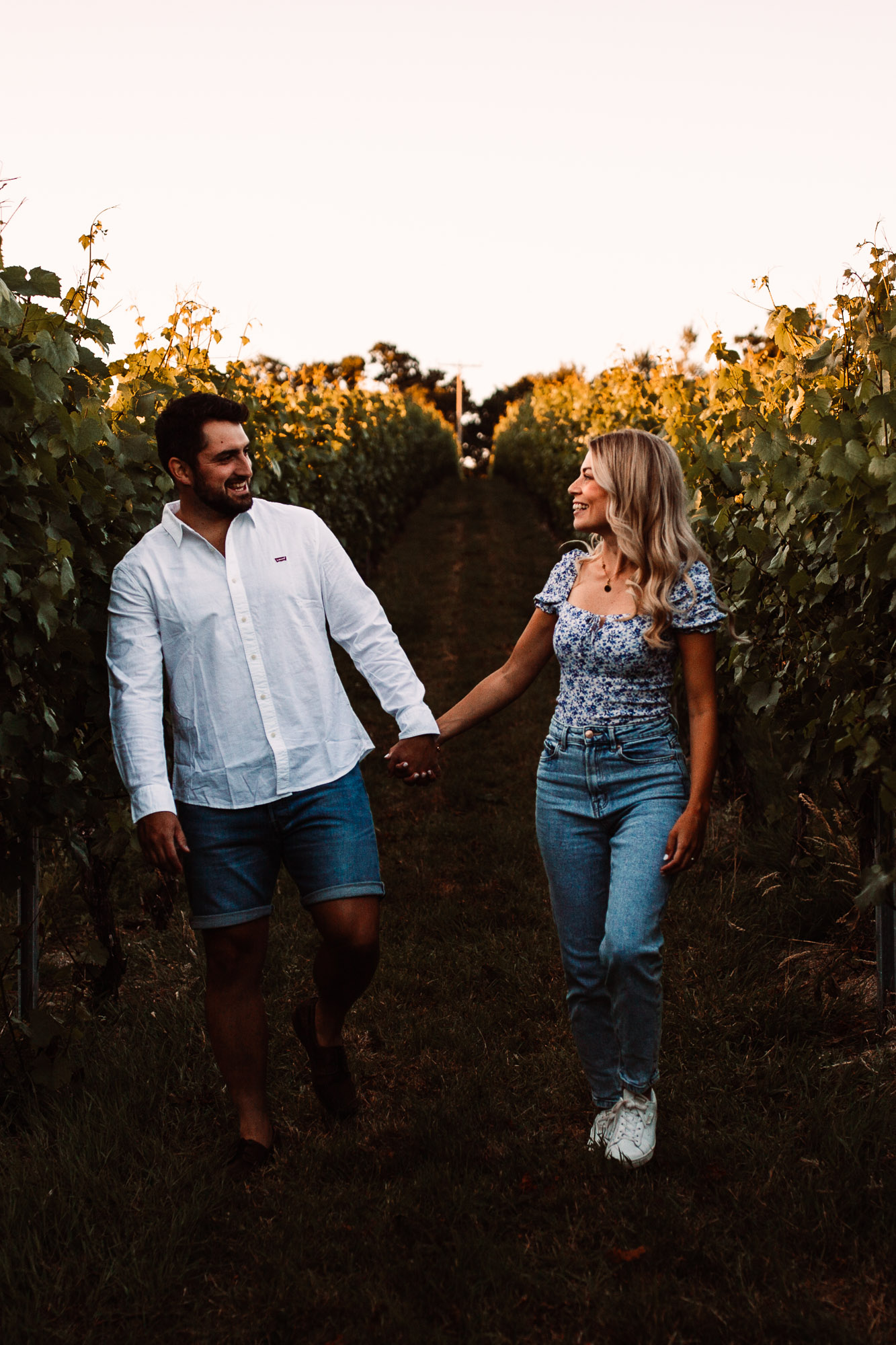 Couple hand in hand wearing jeans and a t shirt running hand in hand inside a vineyard