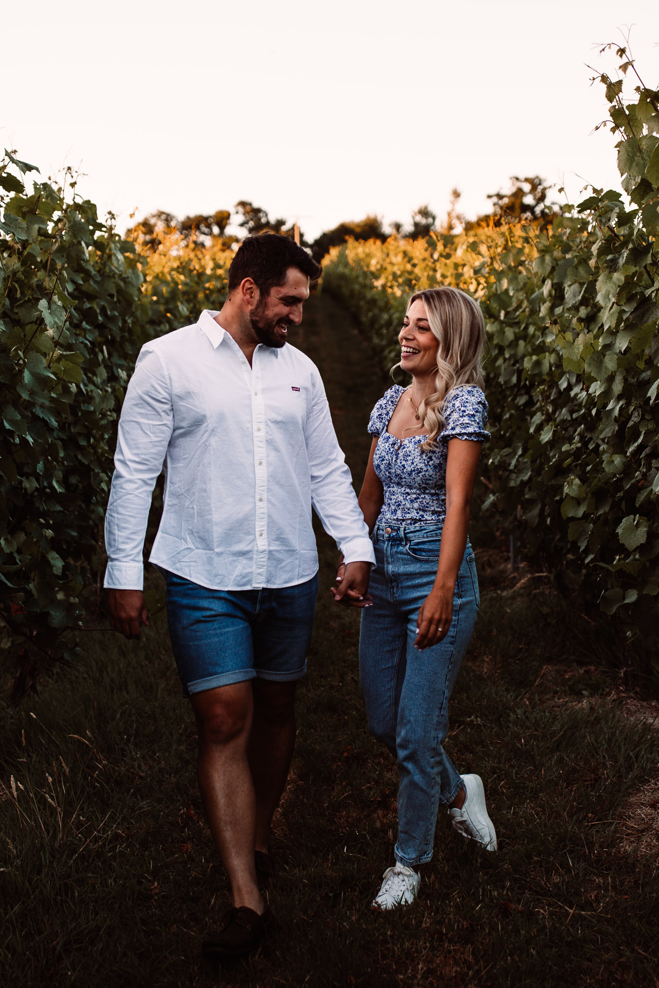 fiances holding hands walking through the vineyards laughing with one another