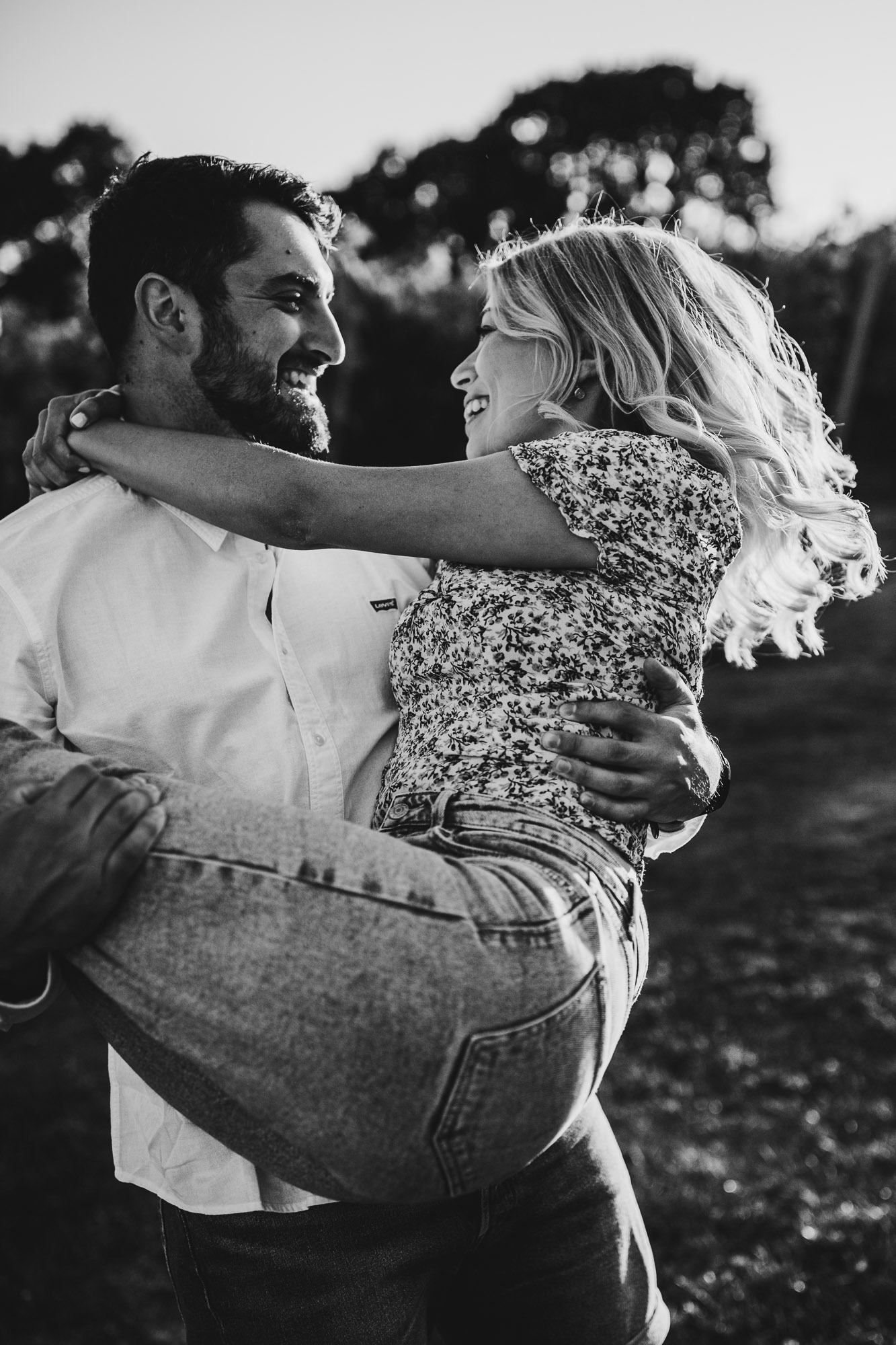 groom to be holding up his fiance in his arms in black and white