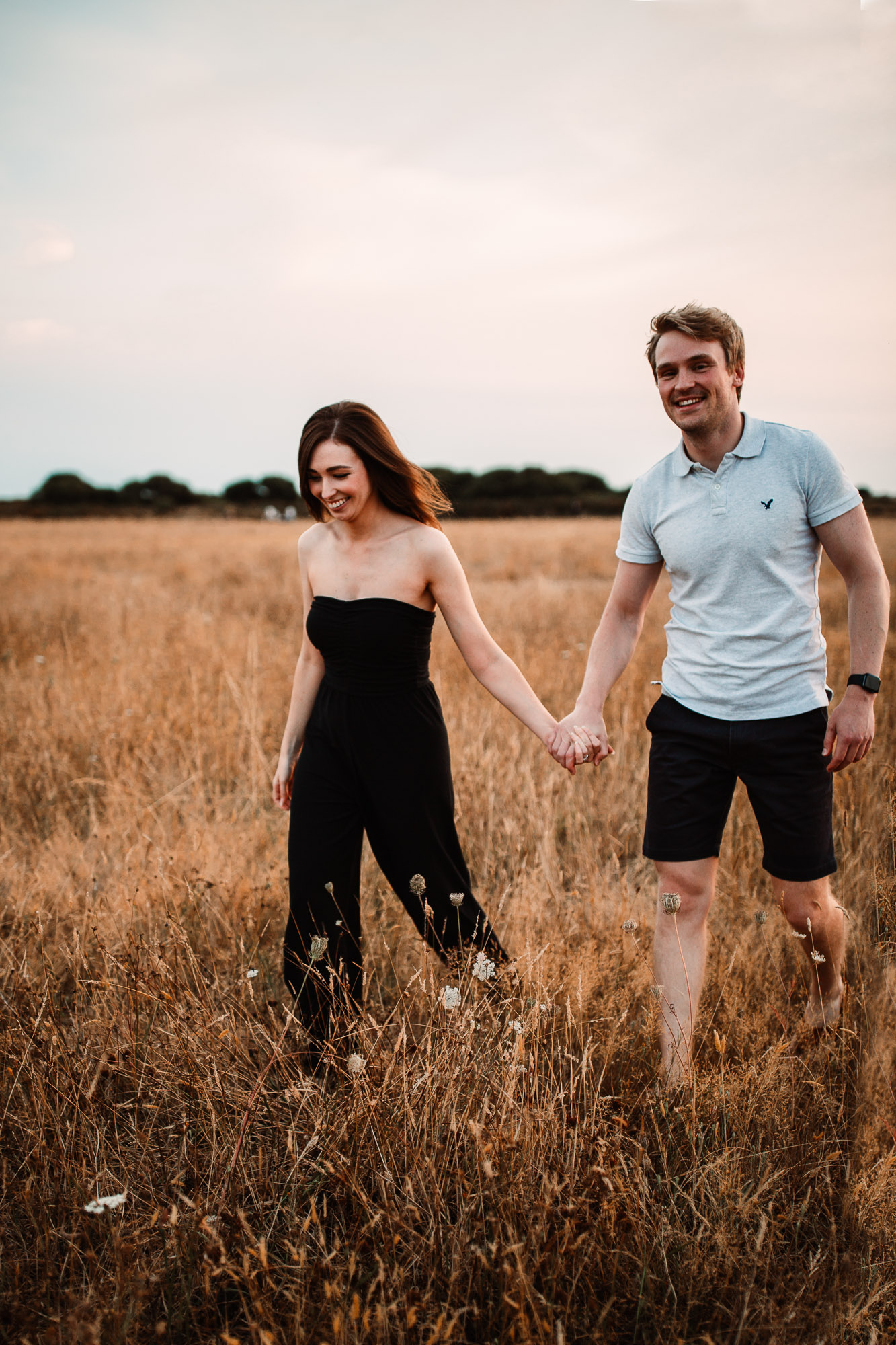 couple walkign hand in hand laughing and smiling in Hengistbury Head 