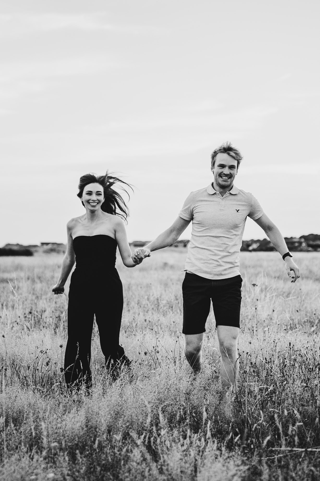 Black and white shot of couple running towards me in a field 