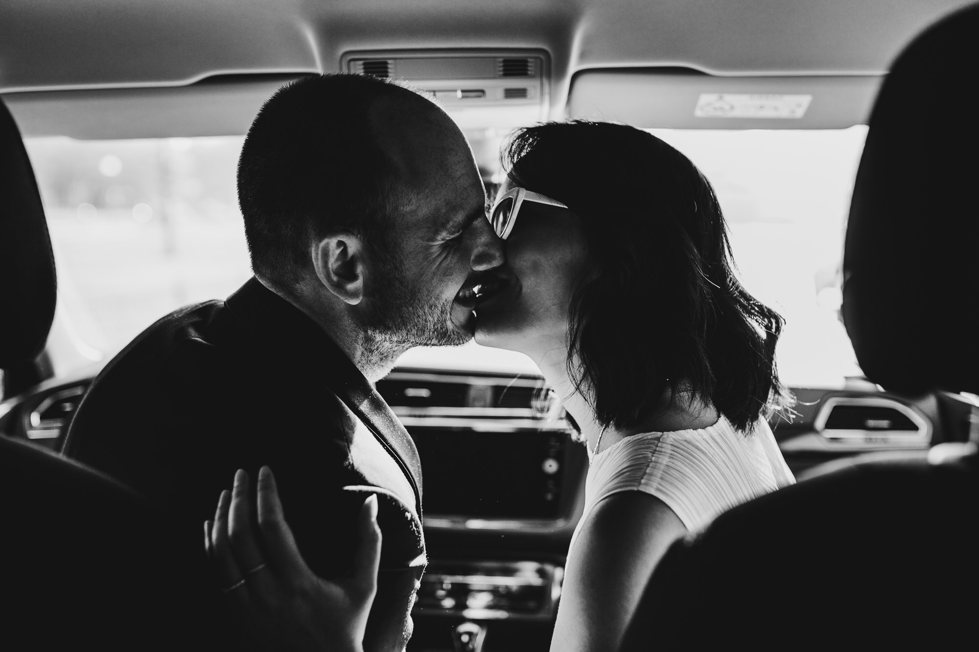 black and white shot of bride and groom kissing in their car