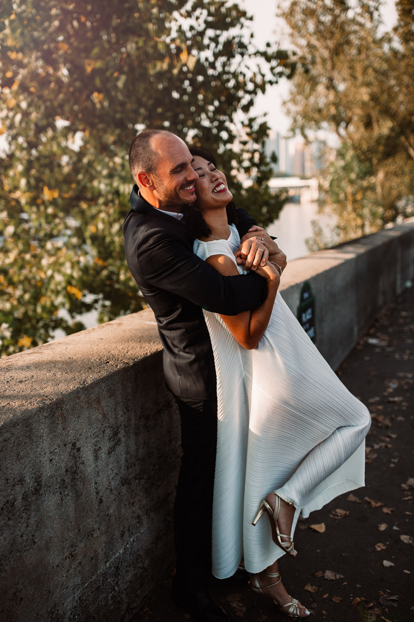 groom and bride leaning against bridge, laughing in paris