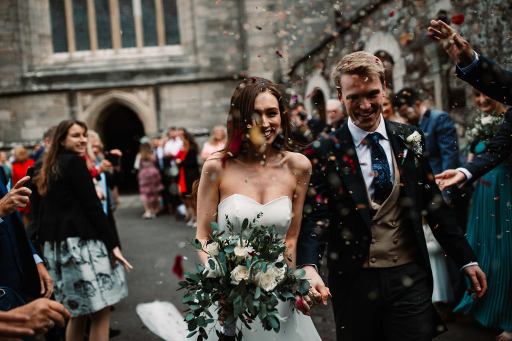 couple hand in hand laughing and smiling as they walk through the confetti