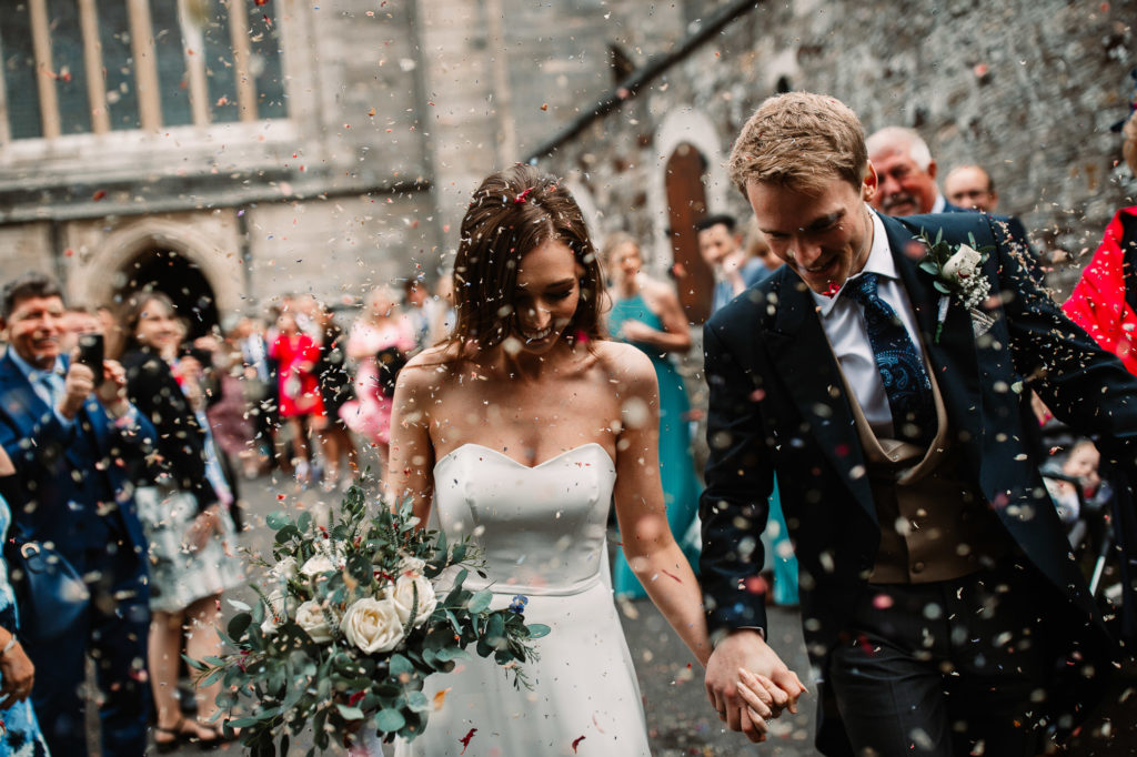 couple hand in hand laughing and smiling as they walk through the confetti