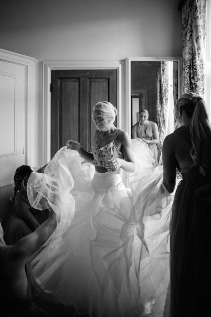 black and white shot of bride putting her dress on at minterne house