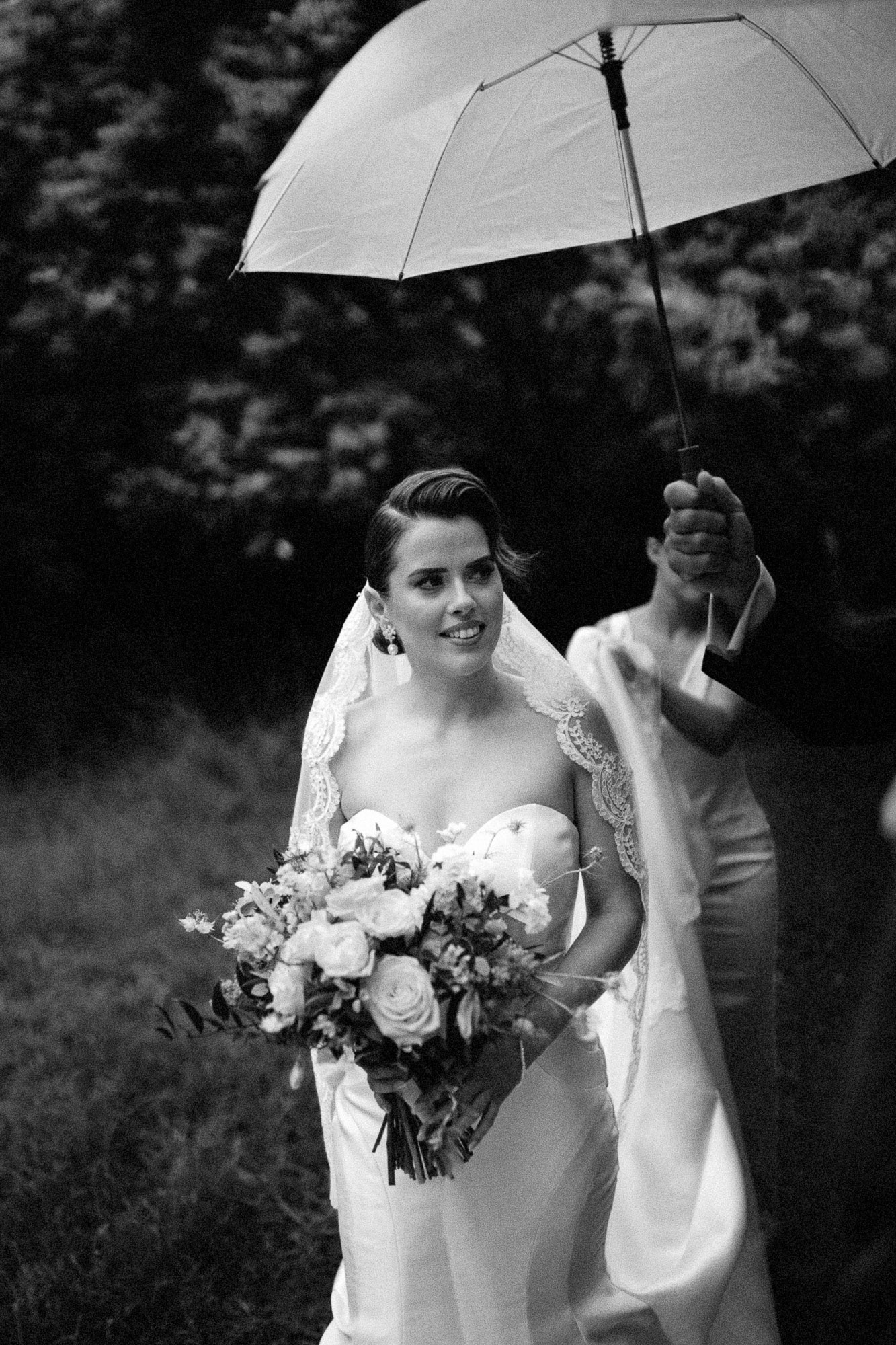 black and white shot of bride under brolly with her dad laughing