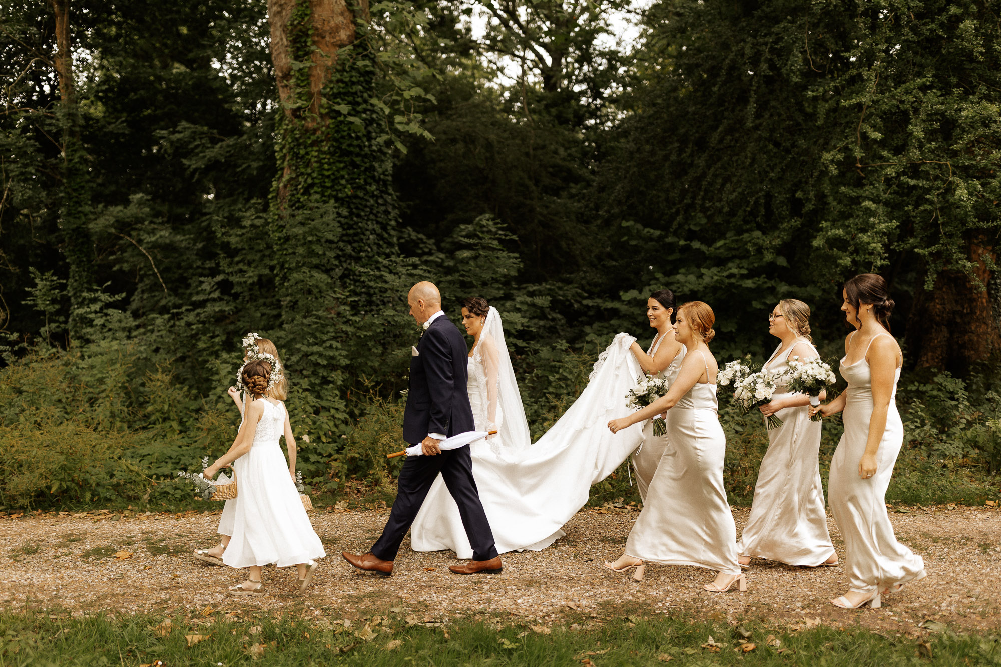 bridal party walking to the ceremony holding dress